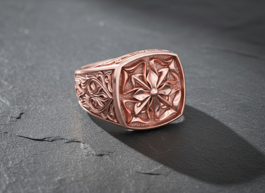 Ornate men's Maltese Cross ring in rose gold, showcasing the detailed floral motif and stippled texture on a slate surface.