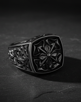 Men's silver Maltese Cross ring with detailed floral scrollwork on the band, shown at an angle on a dark slate surface.