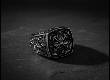 Men's silver Maltese Cross ring with detailed floral scrollwork on the band, shown at an angle on a dark slate surface.