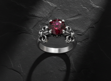 Gold-toned fleur-de-lis ring with deep red ruby displaying intricate crown setting and French heraldic design