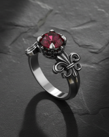 Sterling silver fleur-de-lis ring with red ruby in ornate crown setting on dark slate background