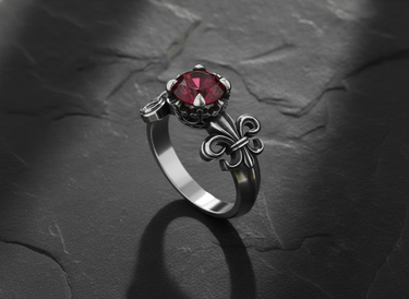 Sterling silver fleur-de-lis ring with red ruby in ornate crown setting on dark slate background