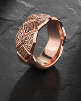 Rose gold version of geometric patterned ring with intricate ornamental designs on dark stone surface