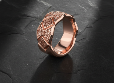 Rose gold version of geometric patterned ring with intricate ornamental designs on dark stone surface