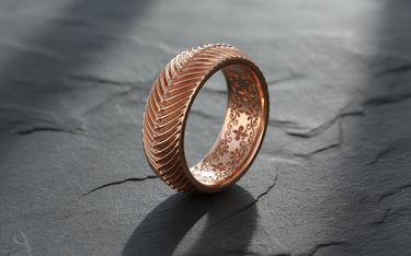 Rose gold herringbone pattern ring with ornate interior filigree work on dark stone background