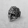 Oxidized silver sugar skull ring showcasing intricate scrollwork and floral details, angled on a textured gray background.