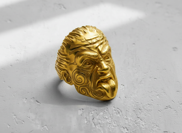 Angled shot of the Maori warrior ring's powerful design, shown here in a luxury gold finish on a textured white surface.