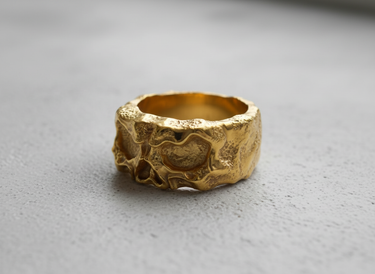 Gold vermeil skull band ring featuring deep eye sockets and rugged texture on grey background
