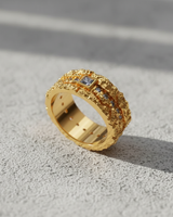 14K gold vermeil textured gemstone ring with a central blue square gem, shown at an angle on a concrete surface.