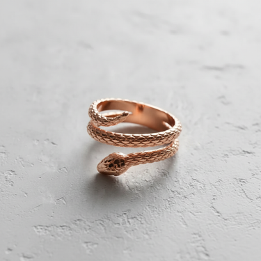 Rose gold finish on a sterling silver snake ring, with a focus on the coiled tail and head, resting on a textured surface.