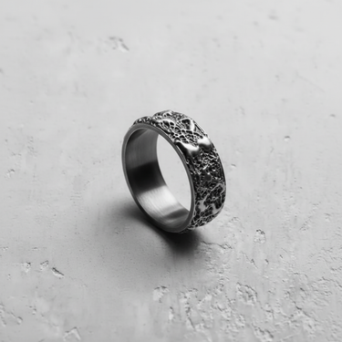 Angled shot of a handcrafted textured silver ring, detailing the abstract raised forms and deep, porous metalwork.