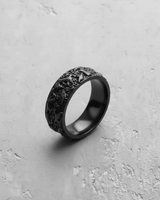 Silver molten texture ring with a matte black rhodium plating, showing its irregular organic surface on a concrete background.
