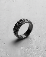 Black rhodium plated Silver Mountain Ring with a rugged rock texture, angled to show its craggy surface on a concrete background.