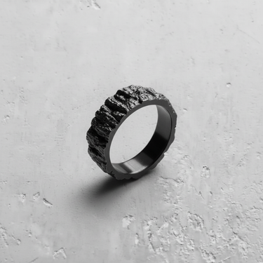 Black rhodium plated Silver Mountain Ring with a rugged rock texture, angled to show its craggy surface on a concrete background.