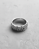 Top-down view of the Silver Mountain Ring, showcasing its irregular, craggy edges and rock texture on a light concrete surface.