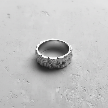 Top-down view of the Silver Mountain Ring, showcasing its irregular, craggy edges and rock texture on a light concrete surface.