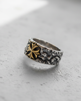 Two-tone silver cross ring with an oxidized textured band and a gold-plated central floral cross emblem, shot from an angle.