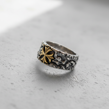 Silver Textured Cross Ring with a gilded floral cross emblem, shown at an angle on a light gray concrete surface.