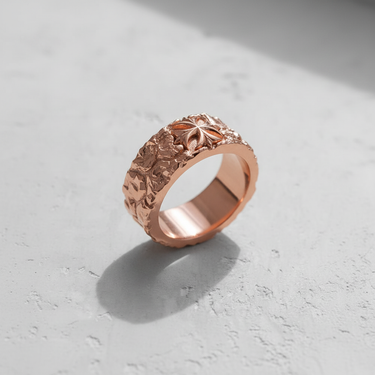 Rose gold plated silver cross ring showcasing its rough, organic band texture and stylized floral cross on a light surface.