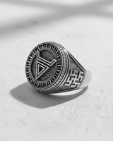 Close-up of the geometric silver ring in black and white, highlighting the textured sunburst face and maze-like side patterns.