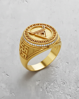 Gold vermeil geometric signet ring with an inverted triangle symbol and sunburst border, shown on a textured surface.