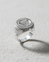 Polished sterling silver geometric symbol ring with an inverted triangle and pave stone halo, shown on a light concrete surface.
