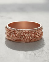 Rose gold plated Silver Wave Grid Ring with ornate scrollwork and a geometric center, shown in soft light on a concrete surface.