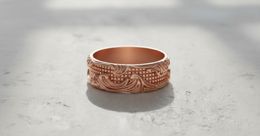 Rose gold plated Silver Wave Grid Ring with ornate scrollwork and a geometric center, shown in soft light on a concrete surface.