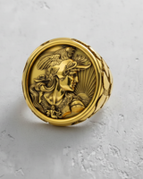 Gold vermeil mythology ring featuring a warrior cameo and rooster helmet, top-down view on a textured white surface.