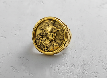 Gold vermeil mythology ring featuring a warrior cameo and rooster helmet, top-down view on a textured white surface.