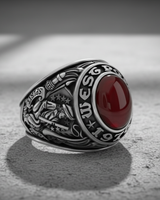 Angled view of a silver vintage class ring featuring a prominent red gemstone and detailed side engravings on a textured surface.