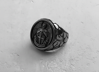 Silver Saint Michael ring showing the detailed archangel relief with shield, sword, and wings on a textured white surface.