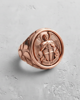 Rose gold plated Saint Michael ring showing the detailed archangel with shield and sword on a light textured surface.