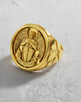 Gold vermeil Saint Michael ring on a textured white surface, showcasing the detailed Archangel, shield, and textured band.