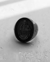 Dramatic studio shot of the Sacred Heart Jesus ring, with shadows emphasizing its bold signet shape and oxidized finish.