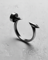 Oxidized silver nail ring with a matte, industrial finish, angled to display the ring's unique bent nail shape and texture.