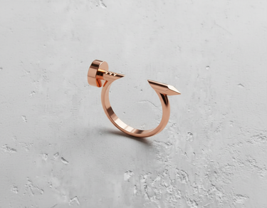 Silver nail ring shown in a polished rose gold finish, detailing the flat nail head and pointed tip on a textured surface.