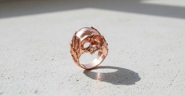 Rose gold plated Silver Skull Wreath Ring on a textured white surface, with a side profile view emphasizing the wreath design.