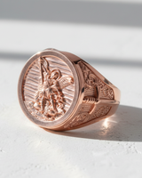 Rose gold plated Archangel Michael ring showing the detailed carving of the angel slaying a demon on a white surface.