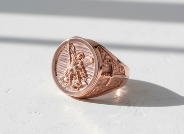 Rose gold plated Archangel Michael ring showing the detailed carving of the angel slaying a demon on a white surface.