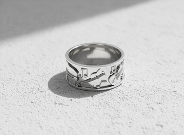 Silver music ring with embossed instruments shown on a bright, textured surface, highlighting its polished sterling silver finish.