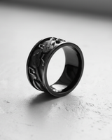 Silver music ring with black rhodium plating, showing embossed musical notes and instruments from an angled side view.