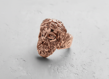 Rose gold plated Silver Zeus Ring with a detailed three-quarter view of the Greek god's face on a textured white surface.