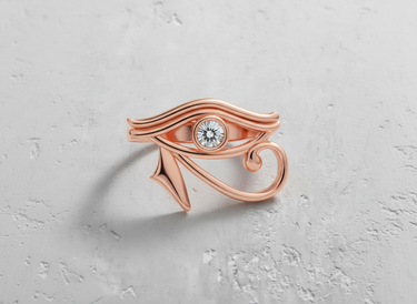 Rose gold Eye of Horus ring featuring a modern, elegant design with a round gemstone, shown on a neutral textured surface.