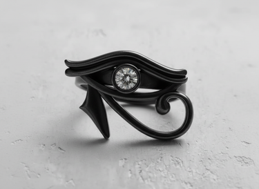 Black rhodium Eye of Horus ring with a central bezel-set gemstone, shown on a light grey textured background.