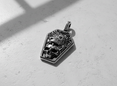 Angled view of the sterling silver lion and skull coffin pendant, highlighting the detailed mane, red gemstone eye, and oxidized finish.