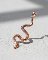 Rose gold plated silver snake pendant with hexagonal scale pattern standing upright on textured grey background