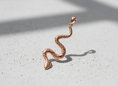 Rose gold plated silver snake pendant with hexagonal scale pattern standing upright on textured grey background