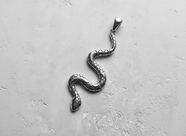 Silver snake pendant with an oxidized hexagonal scale pattern, shown from above on a light grey textured surface.