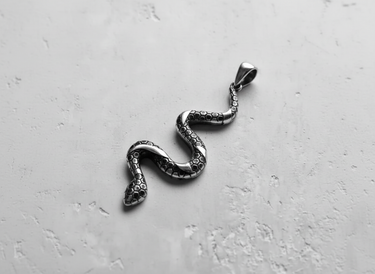Angled close-up of handcrafted silver serpent pendant showing intricate hexagonal texture and polished bail